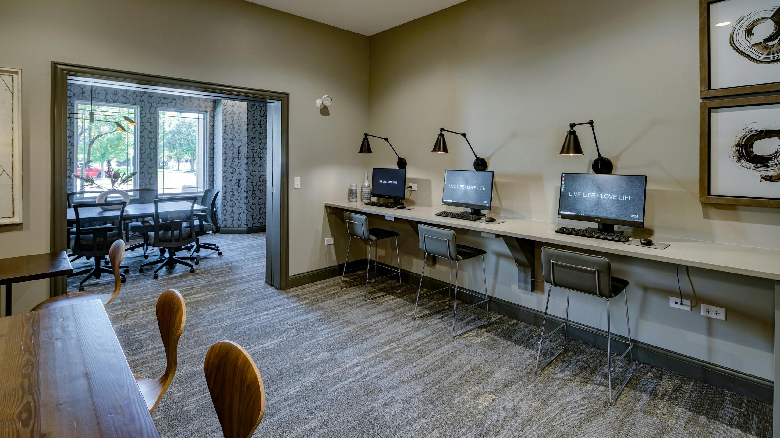 Business center at AMLI at Seven Bridges with 3 computer stations with mounted lights above and view into conference room