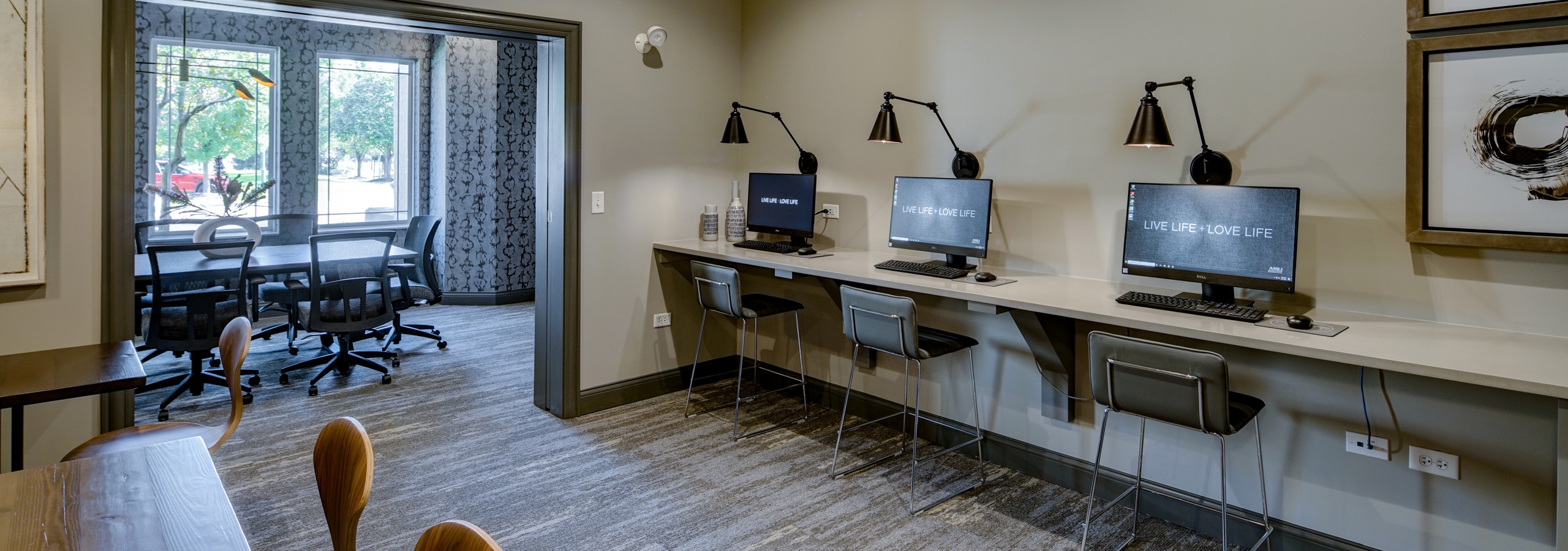 Business center at AMLI at Seven Bridges with 3 computer stations with mounted lights above and view into conference room