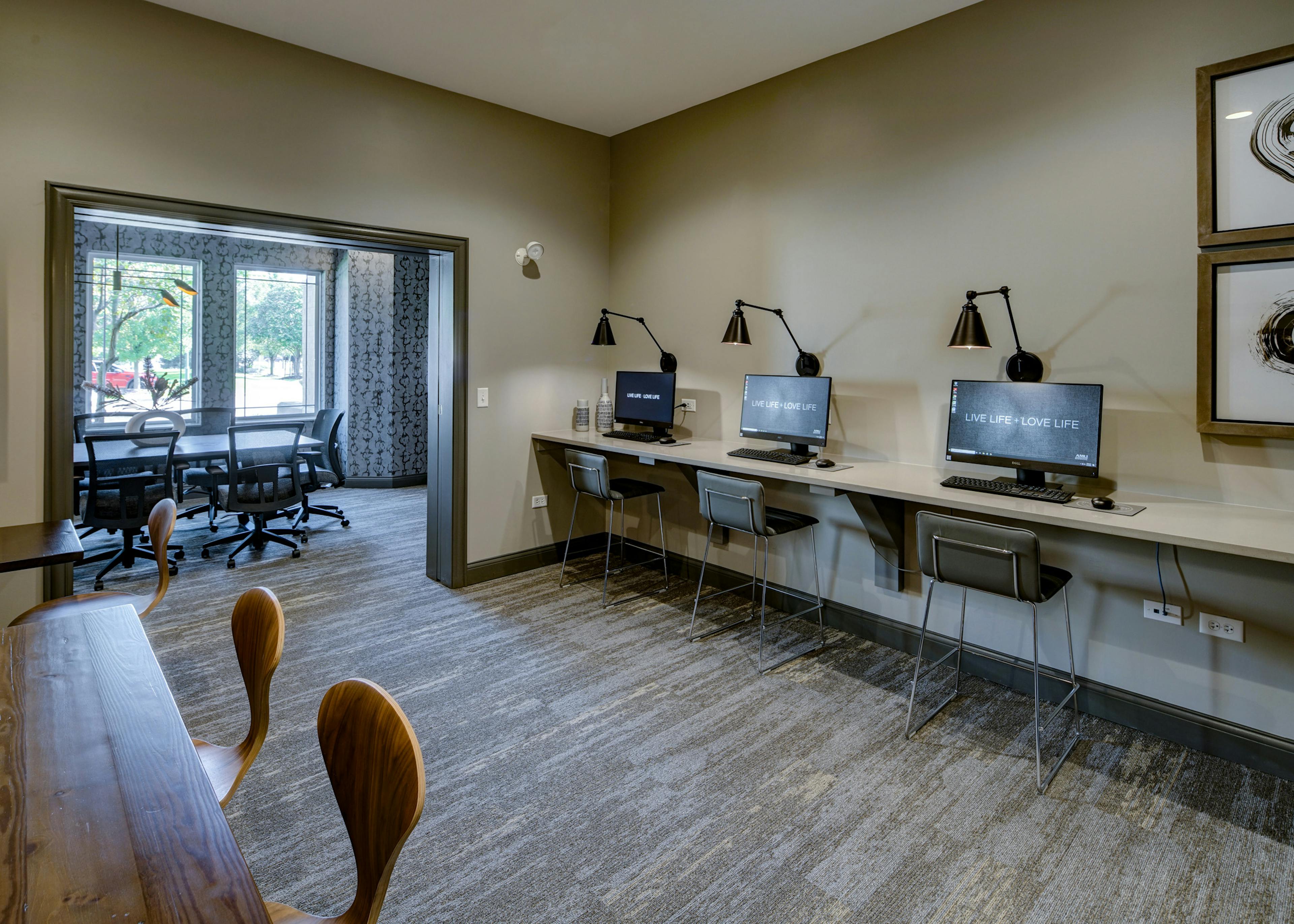 Business center at AMLI at Seven Bridges with 3 computer stations with mounted lights above and view into conference room