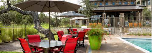 Poolside dining area with dark red seating, white umbrellas, and orange potted plants nearby