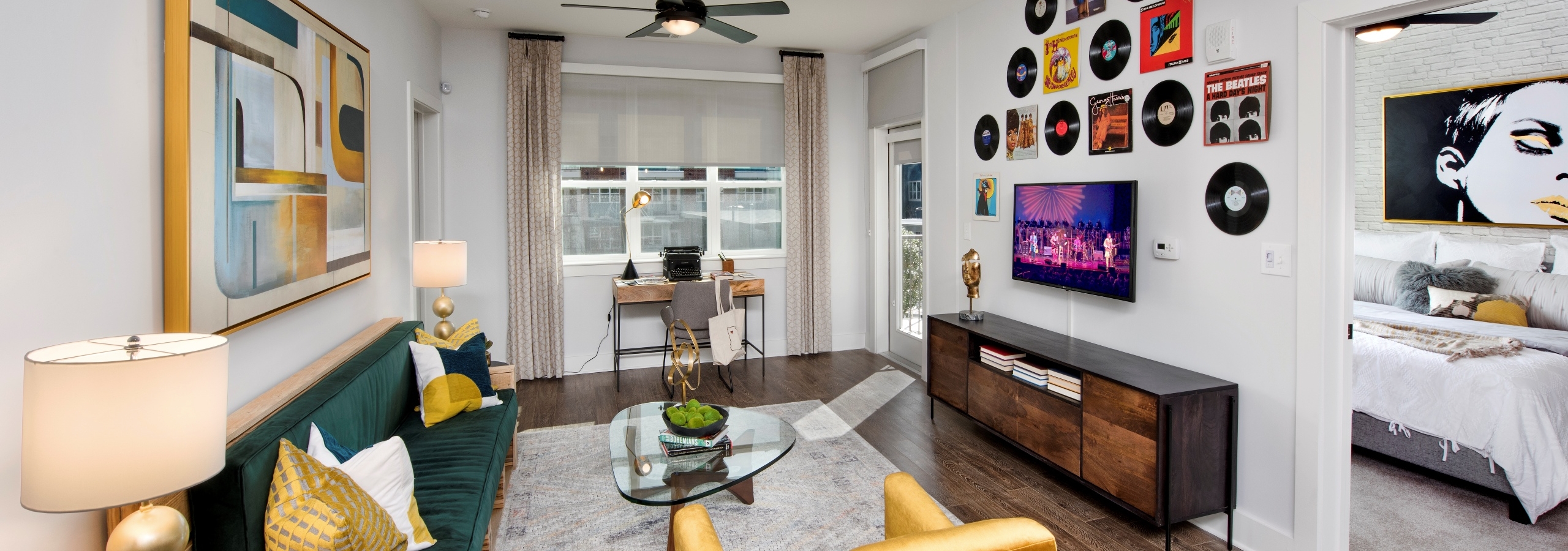 Interior view of AMLI Decatur apartment living room with furniture and ceiling fan and peek inside bedroom through open door