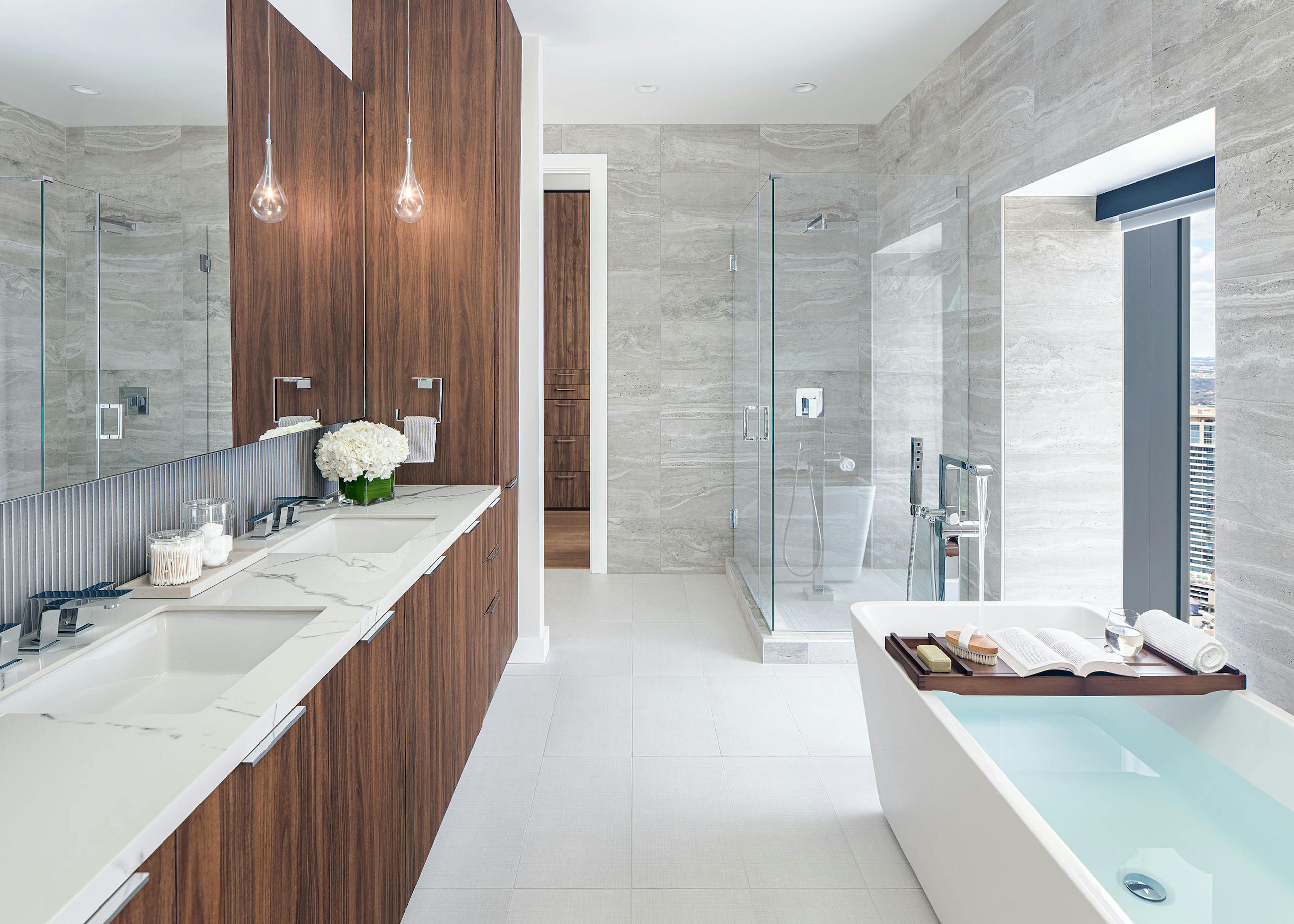 Interior view of AMLI Fountain Place penthouse bathroom with double vanity with dark brown cabinetry and glass shower and tub
