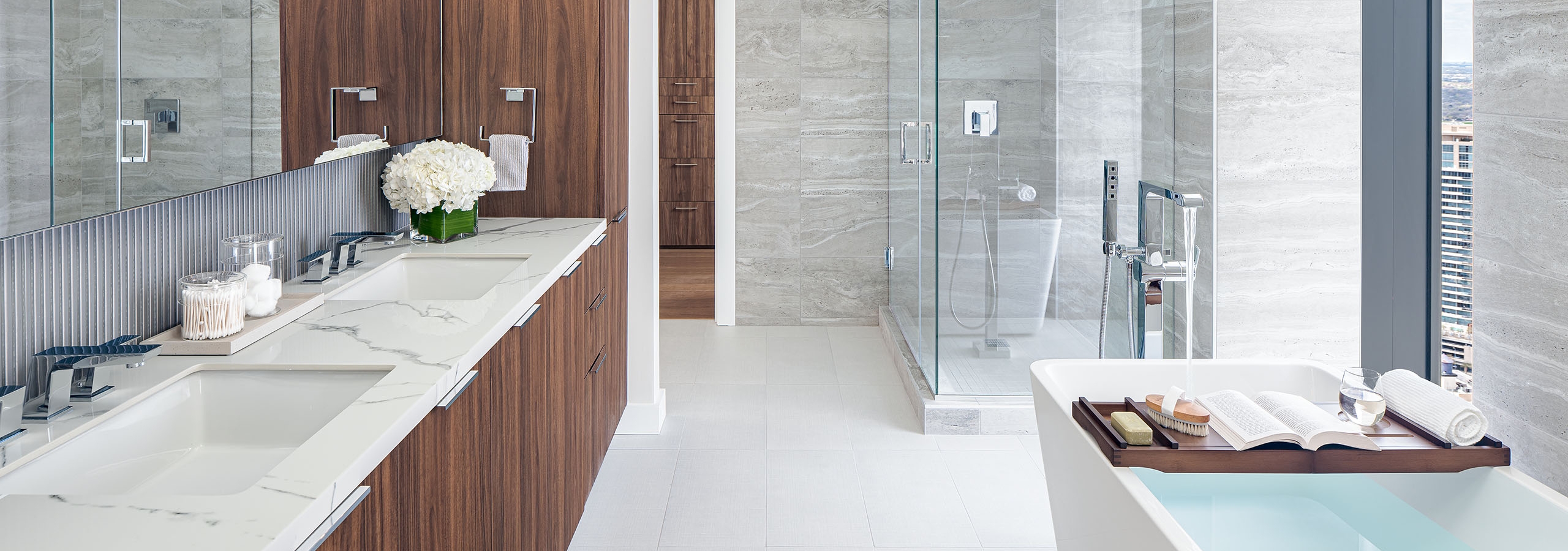 Interior view of AMLI Fountain Place penthouse bathroom with double vanity with dark brown cabinetry and glass shower and tub