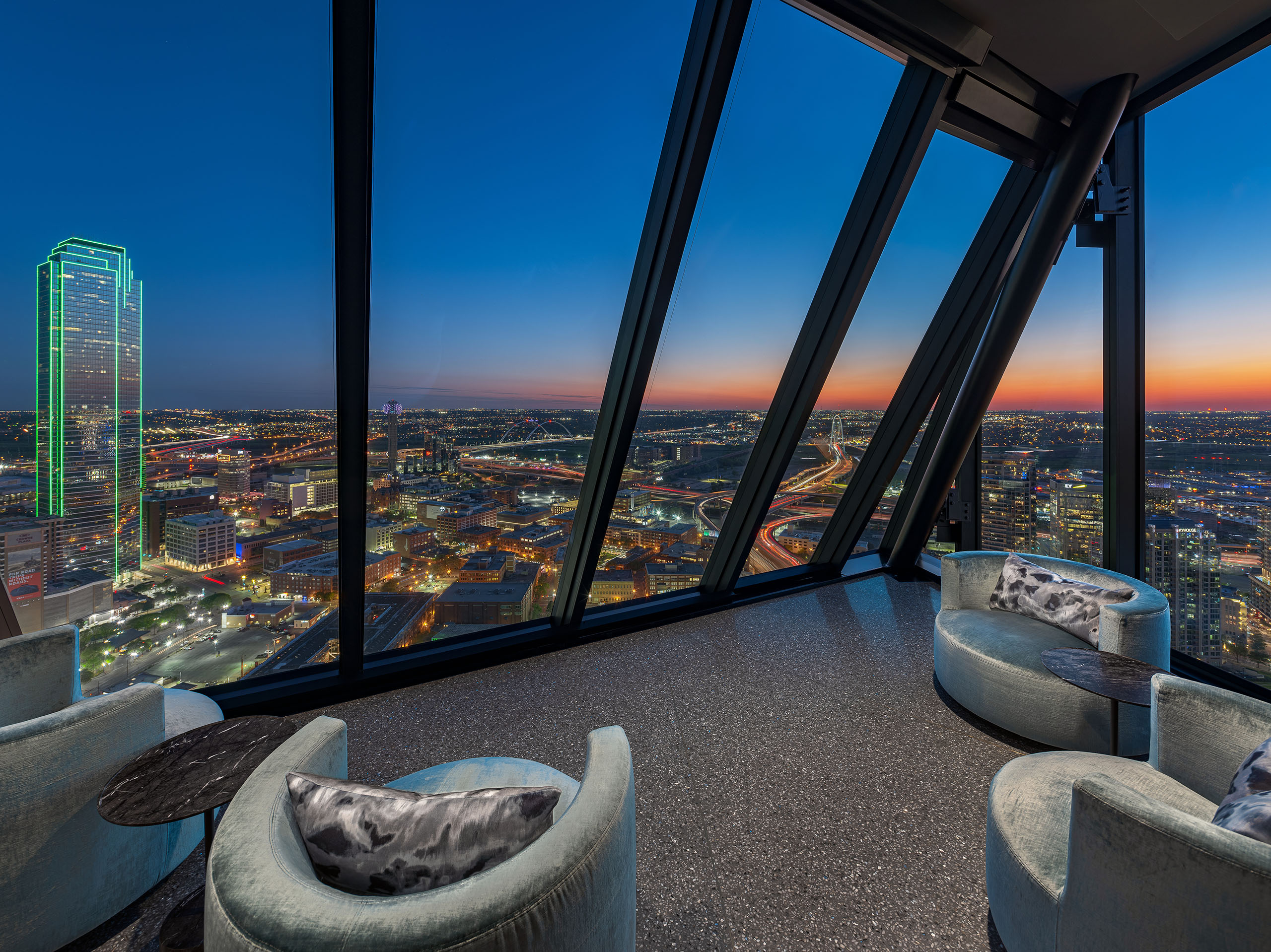AMLI Fountain Place sky lounge with 3 gray velvet chairs overlooking night skyline with city lights form expansive windows