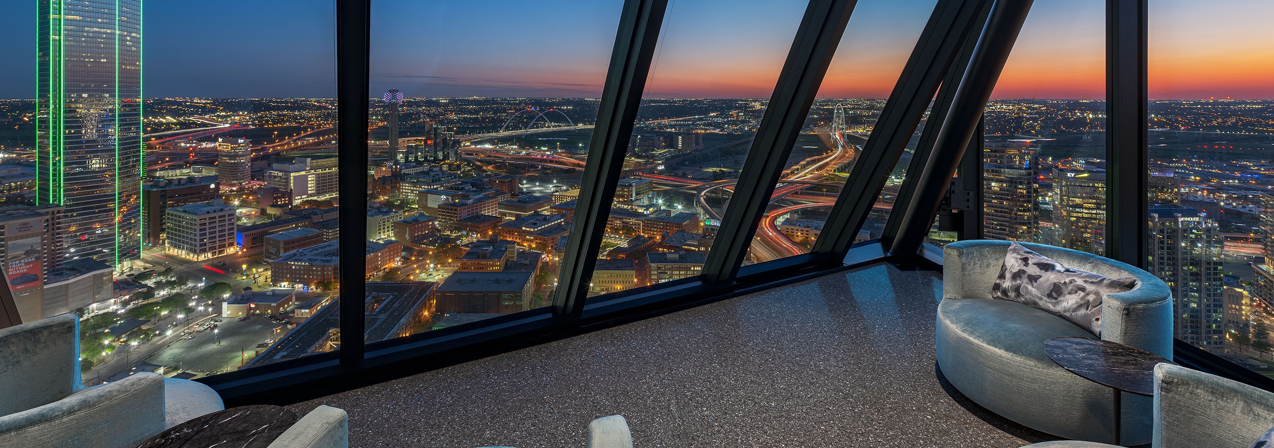AMLI Fountain Place sky lounge with 3 gray velvet chairs overlooking night skyline with city lights form expansive windows