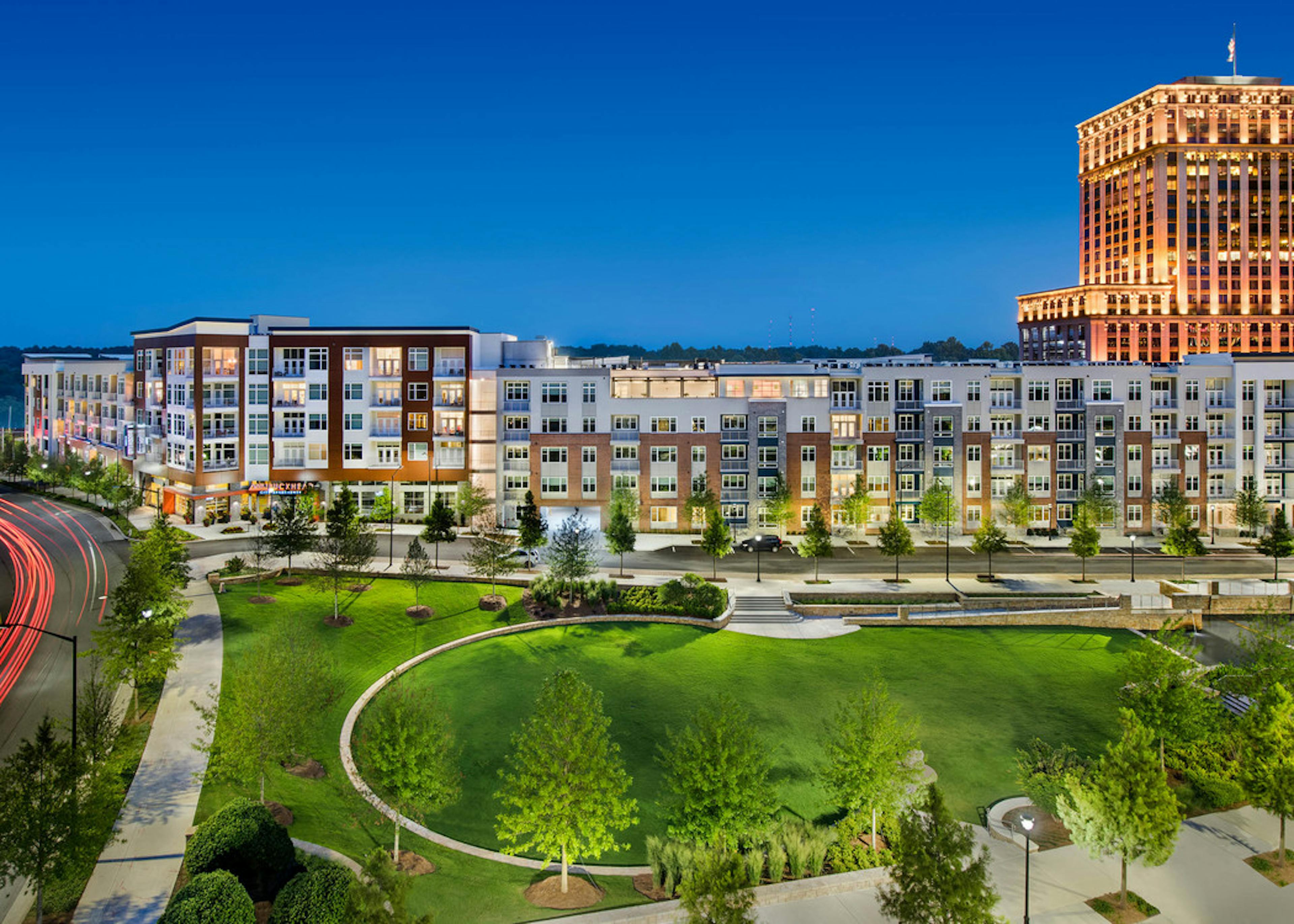 Exterior of AMLI Buckhead apartment community at night with light coming through the windows and trees lining the sidewalk