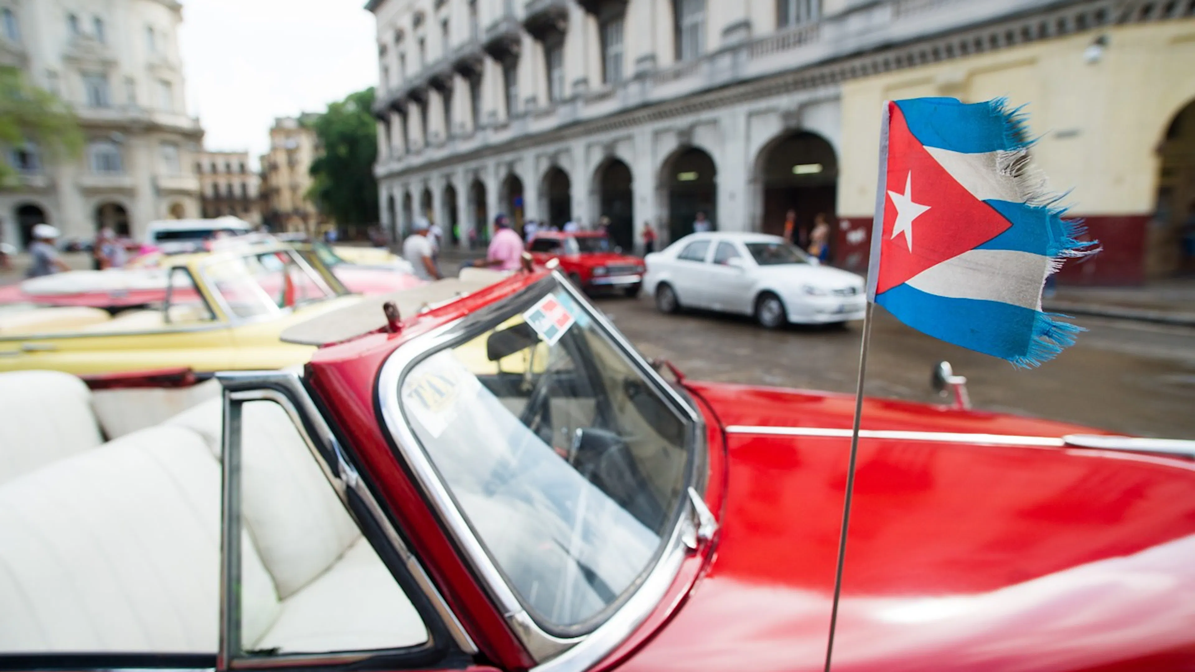 A small Cuban flag flying on the antenna of a vintage red car on the streets of Cuba