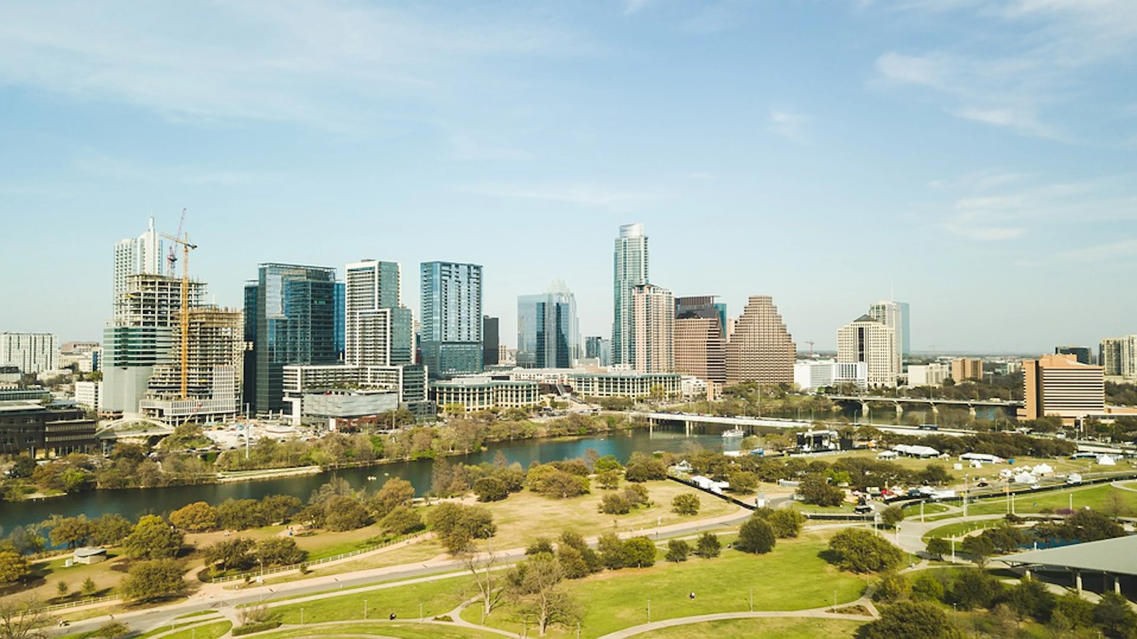 Austin skyline with grass and trees in foreground and Lady Bird Lake meandering in front of city buildings in background