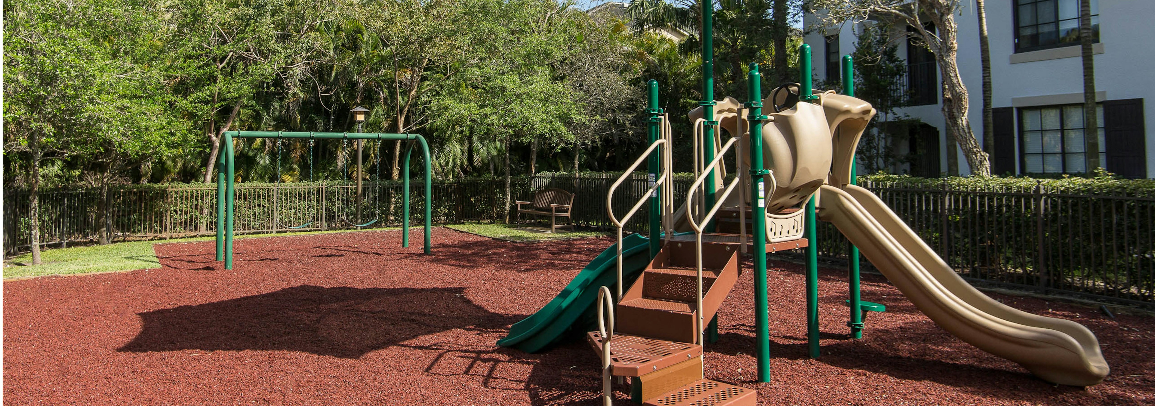 Outdoor children’s playground at AMLI Toscana Place featuring stairs for climbing, slide and swings all set on rubber floor