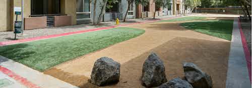 Daytime view of Dog Park with gravel trim, grass and esthetic boulders and pet waste station at AMLI Warner Center apartments