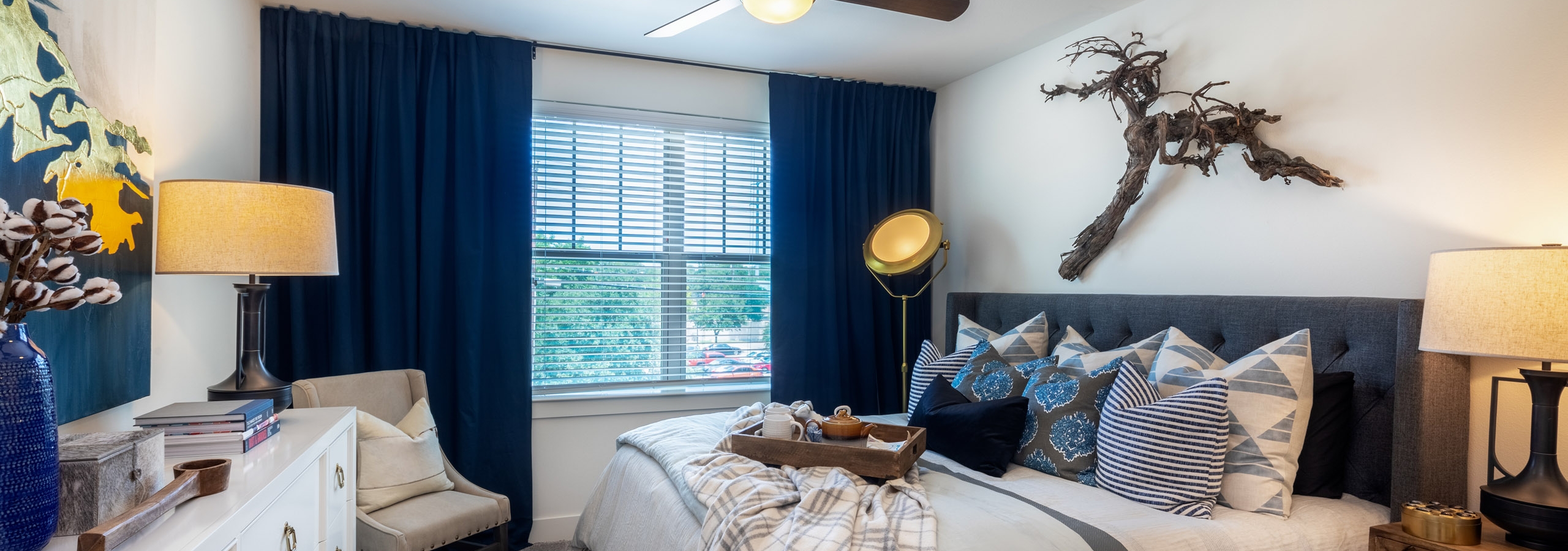 AMLI Grapevine apartment bedroom with gray carpet and a ceiling fan and a large window with blinds and dark blue curtains