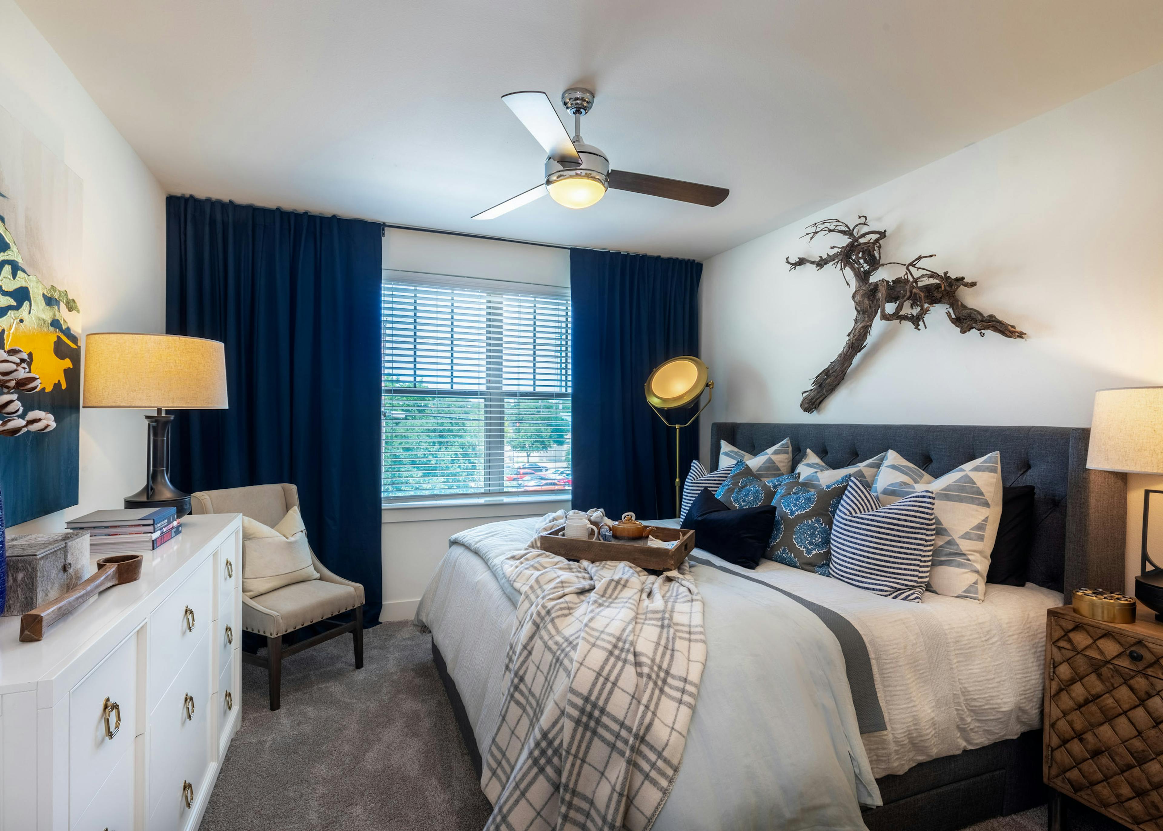 AMLI Grapevine apartment bedroom with gray carpet and a ceiling fan and a large window with blinds and dark blue curtains