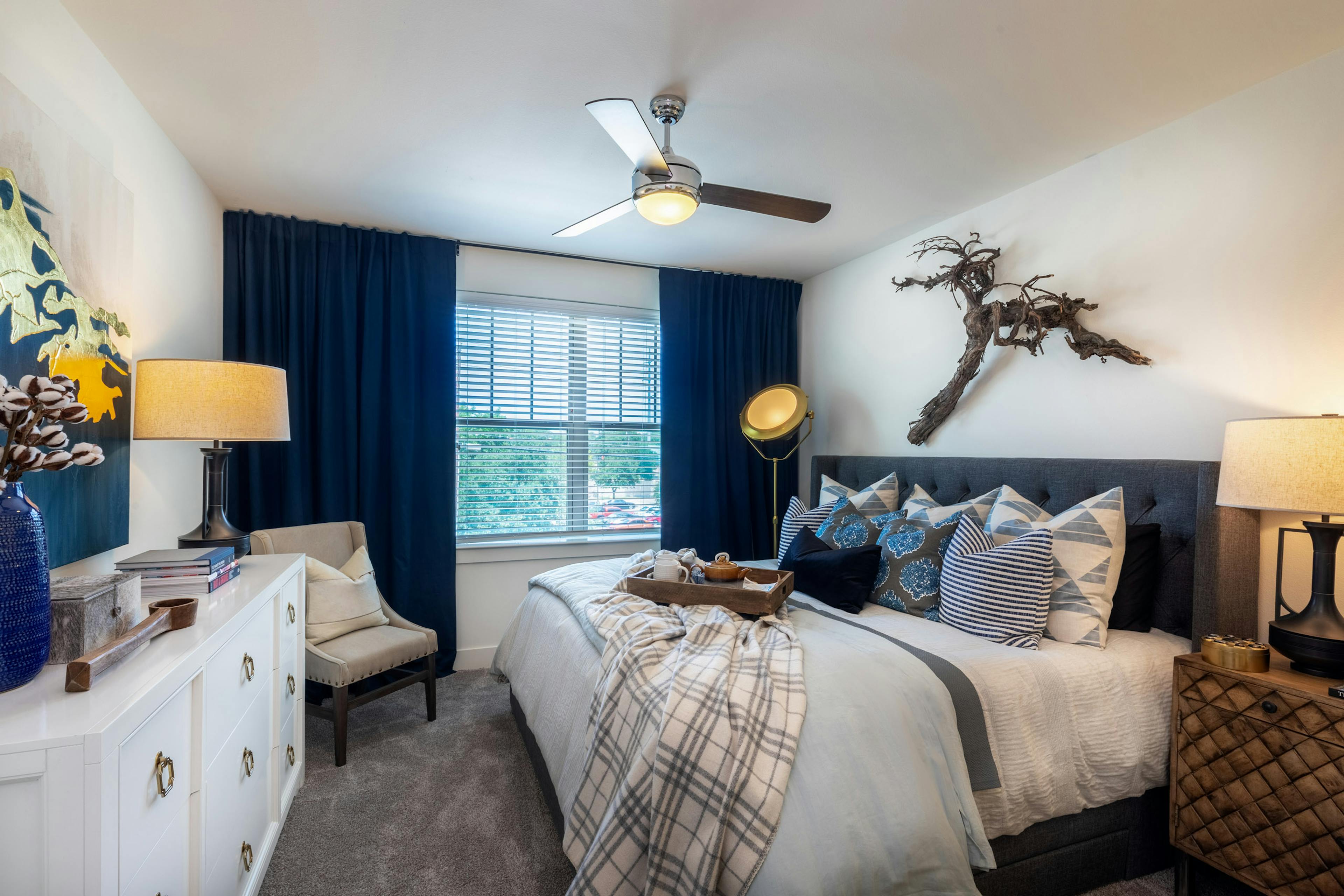 AMLI Grapevine apartment bedroom with gray carpet and a ceiling fan and a large window with blinds and dark blue curtains