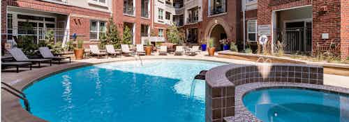 A daytime view of the pool at AMLI Park Avenue apartments with a hot tub and lounge chairs with surrounding trees and plants