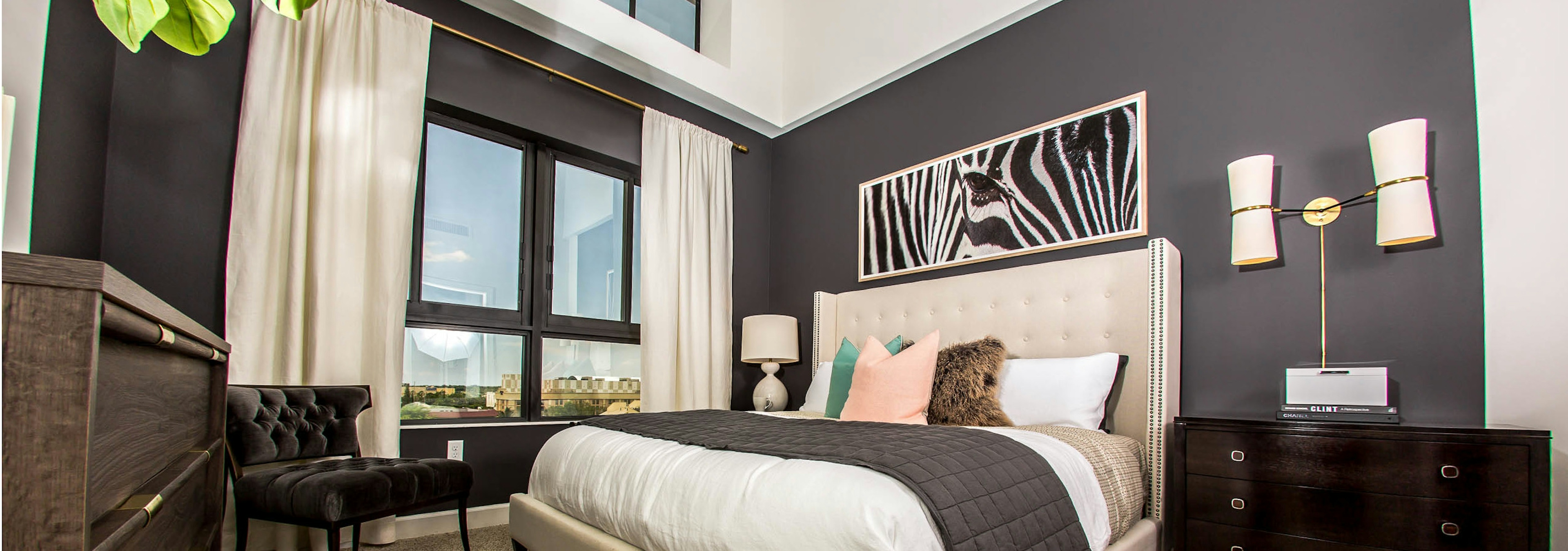 Interior view of an AMLI Joya apartment bedroom with a bed underneath black and white wall art and open window to a sky view