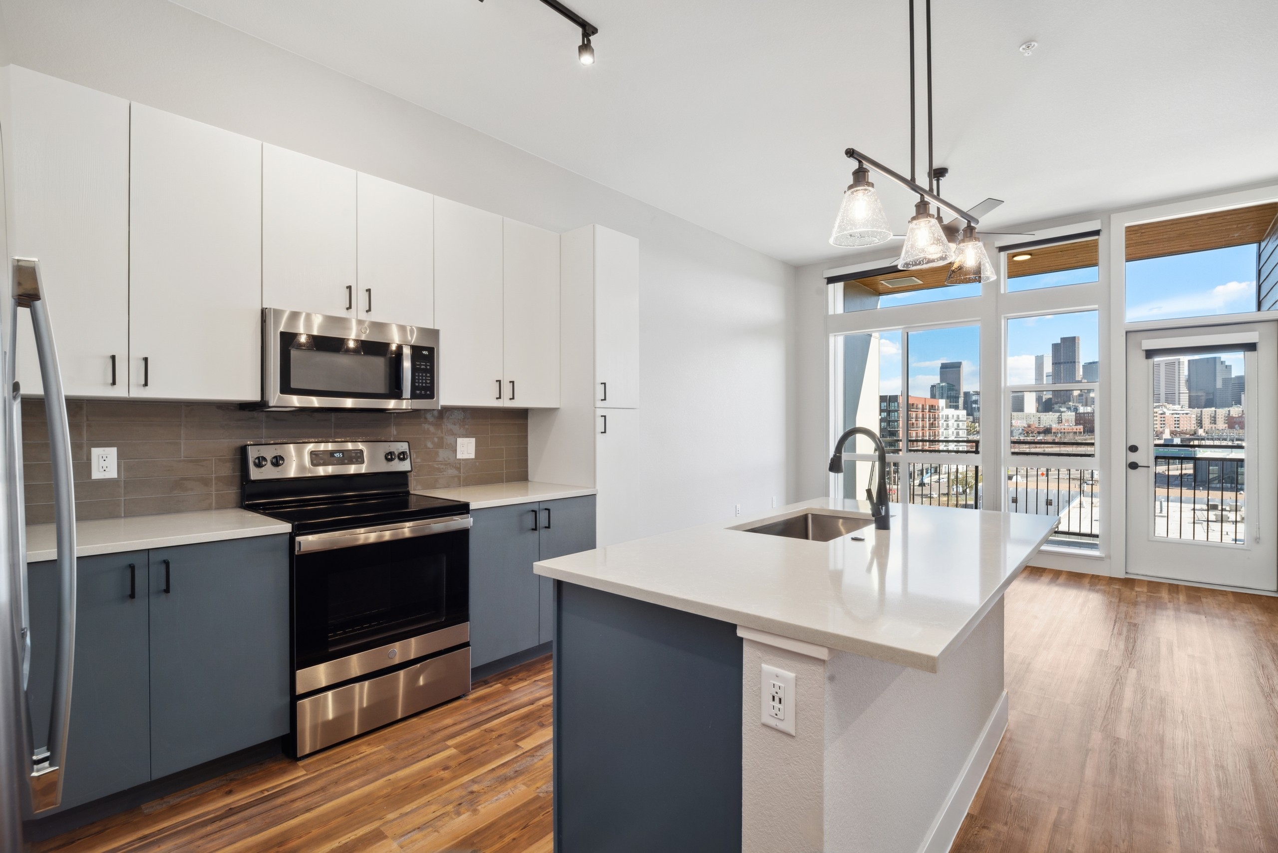 AMLI RiNo apartment kitchen with floor to ceiling windows and skyline view with grey and white cabinets and wood flooring