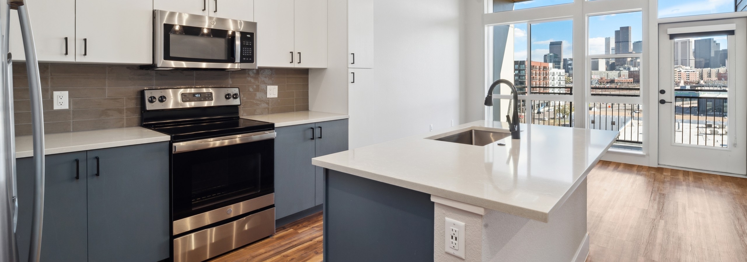 AMLI RiNo apartment kitchen with floor to ceiling windows and skyline view with grey and white cabinets and wood flooring