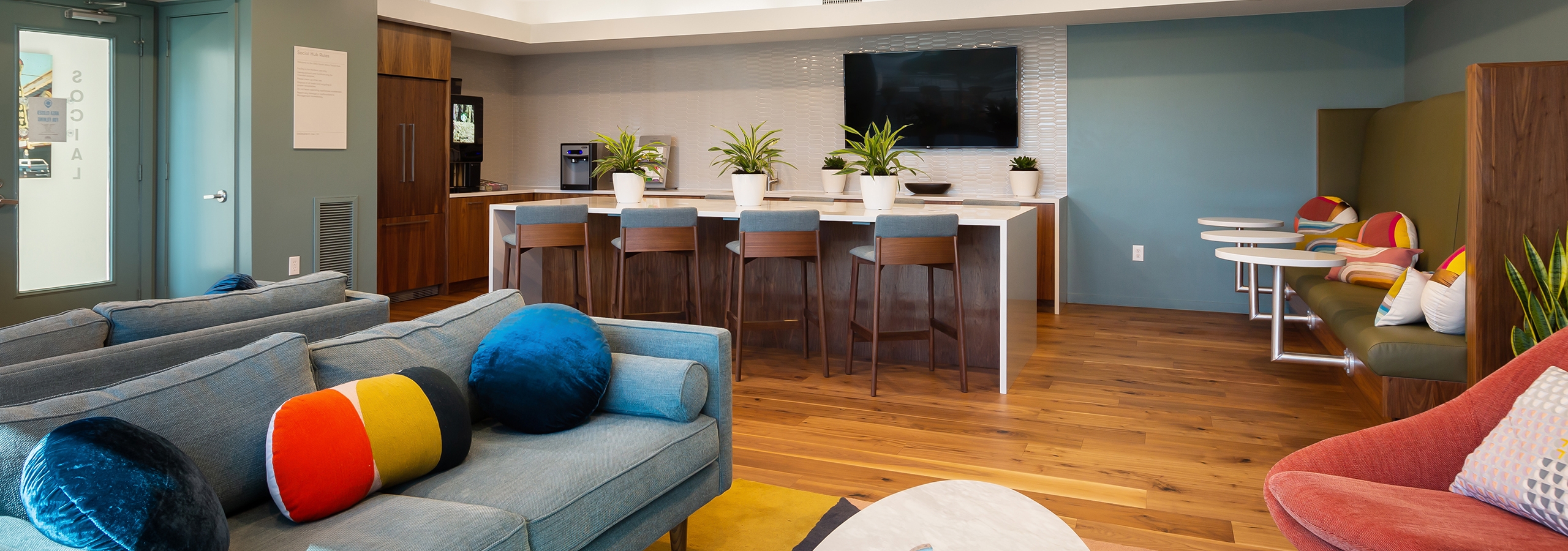 Newly designed clubroom at AMLI South Shore with hardwood flooring and grey walls with blue grey couch and barstool seating