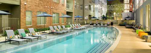 Close up of long swimming pool at AMLI at Mueller with colorful pillows on light lounge chairs along one side of the water