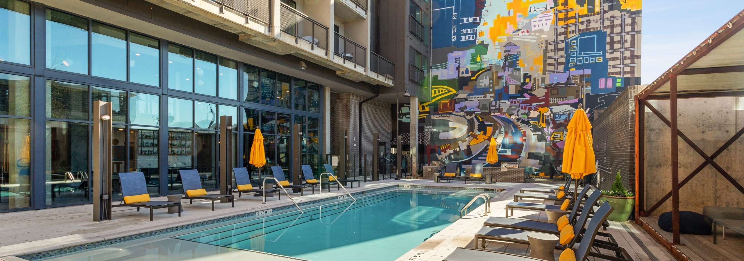 Sunny view of clear salt water pool at AMLI Westside apartments with several lounge seating arrangements and yellow umbrellas