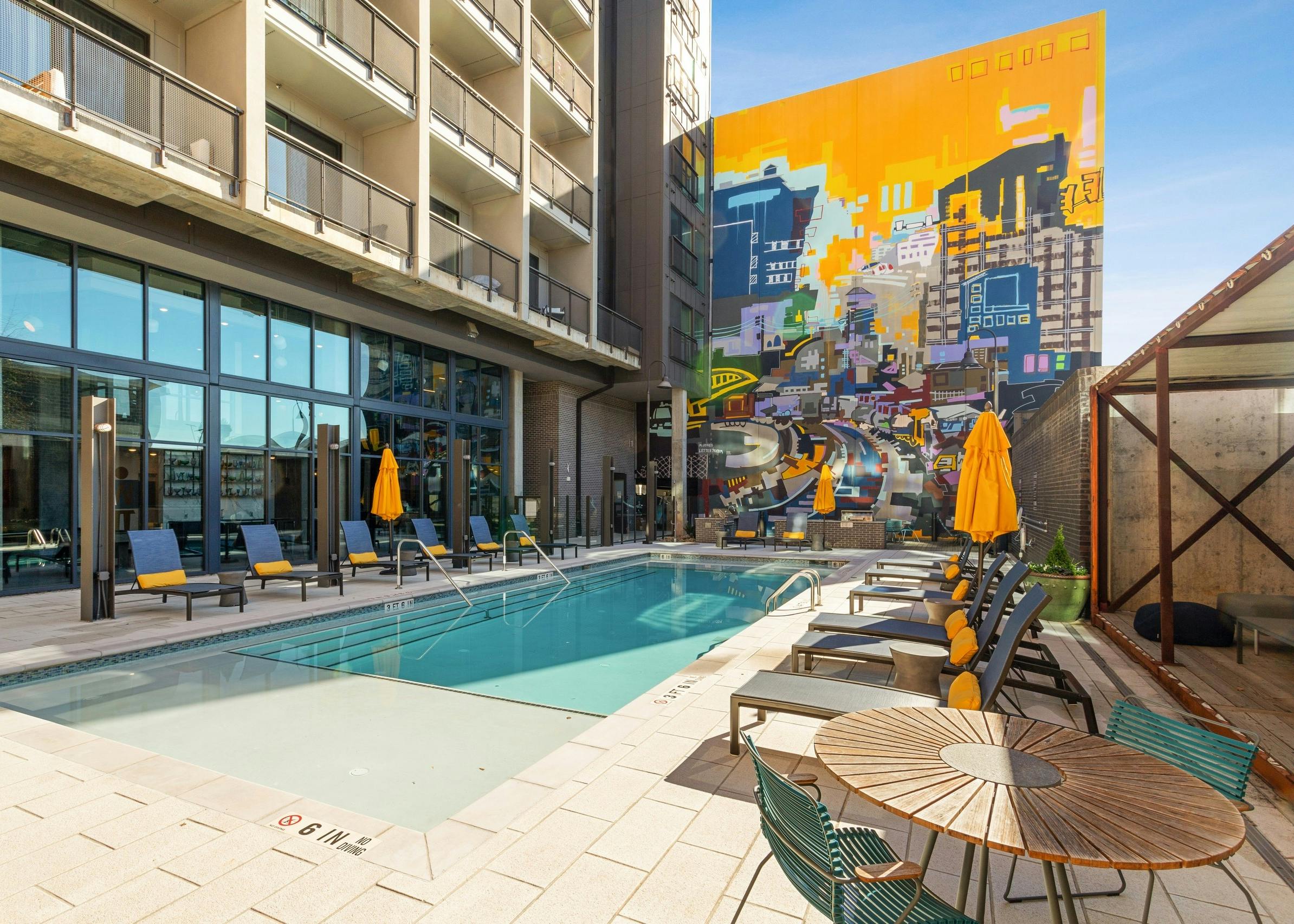 Salt water pool at AMLI Westside apartments with plentiful lounge seating and yellow accent pillows overlooking colorful mural