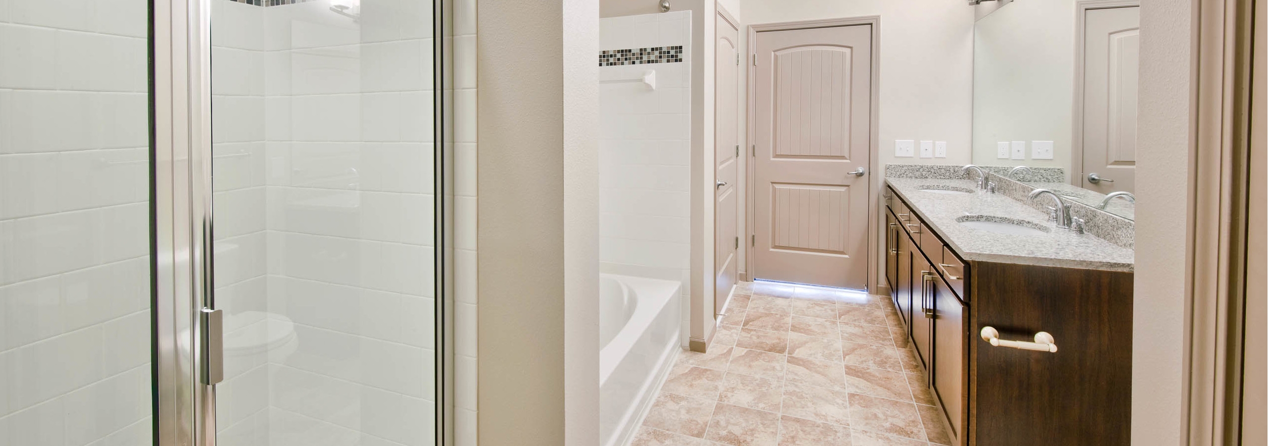Bathroom at AMLI North Point with a double vanity sink and a white tiled bathtub next to a shower with frosted glass doors