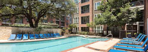 Exterior view of pool on a sunny day at AMLI Eastside with surrounding bright blue lounge chairs and vibrant trees