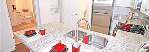 Interior view of AMLI Warner Center apartment kitchen with granite countertops, upgraded cabinets and peek into bathroom area