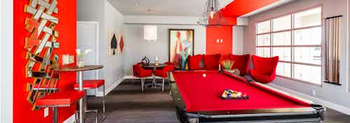 Interior view of the game room at AMLI Arista apartments featuring a pool table and several chairs with a red color scheme