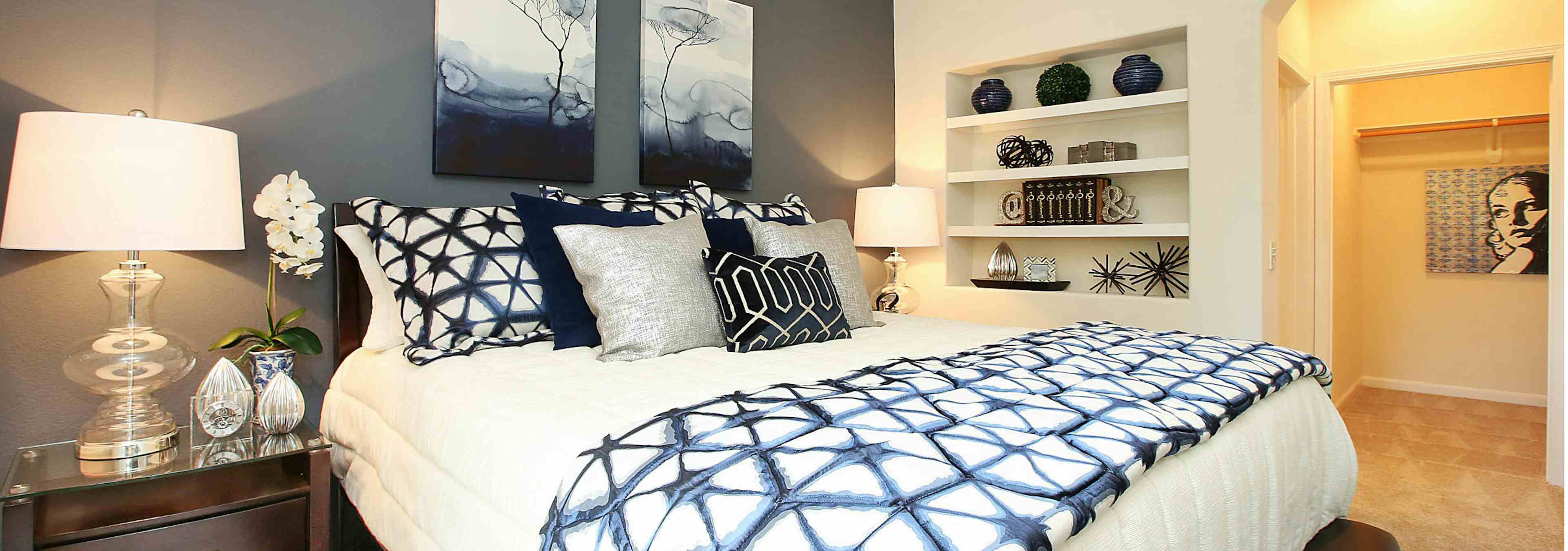 Interior of AMLI Warner Center apartment bedroom with king size bed with decorative pillows, built-in bookshelf and closet