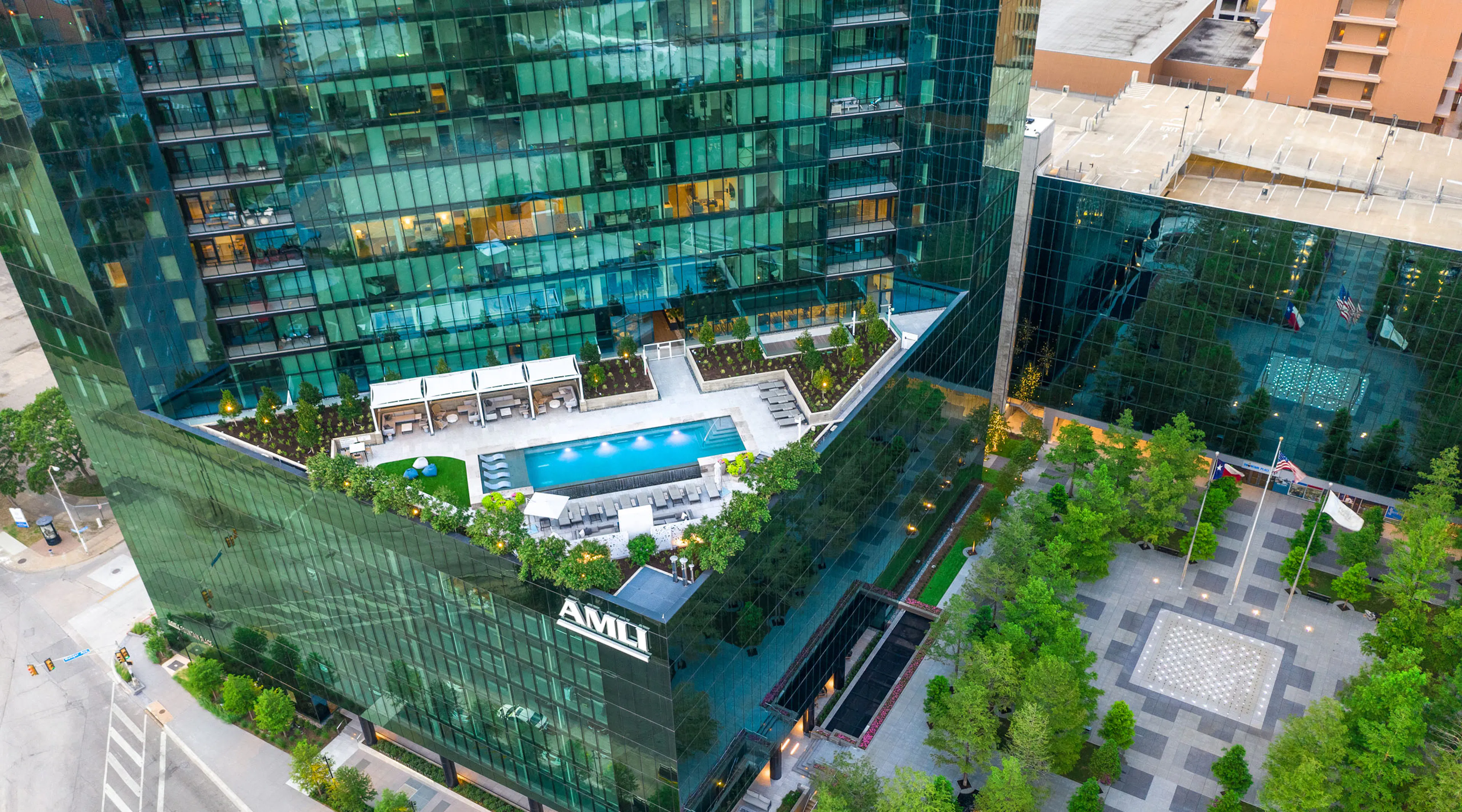 Aerial view of landscaped rooftop pool deck and cabanas at AMLI Fountain Place apartment building with tree lined plaza below