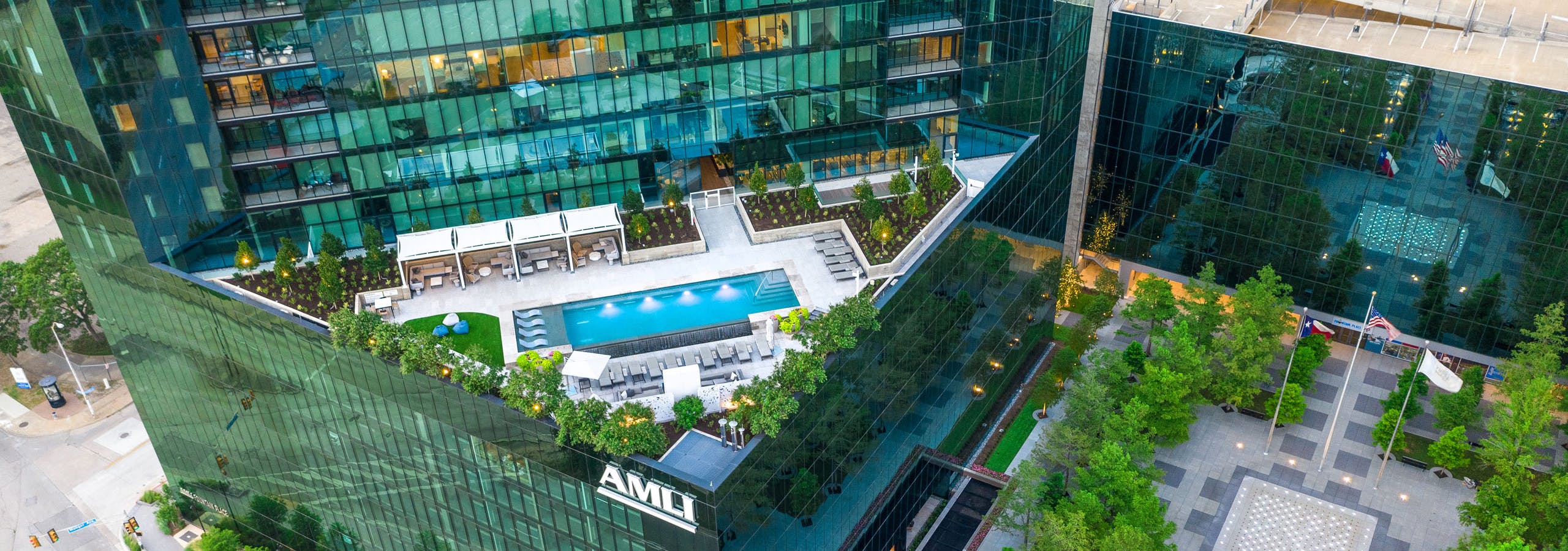 Aerial view of landscaped rooftop pool deck and cabanas at AMLI Fountain Place apartment building with tree lined plaza below