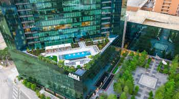 Aerial view of landscaped rooftop pool deck and cabanas at AMLI Fountain Place apartment building with tree lined plaza below