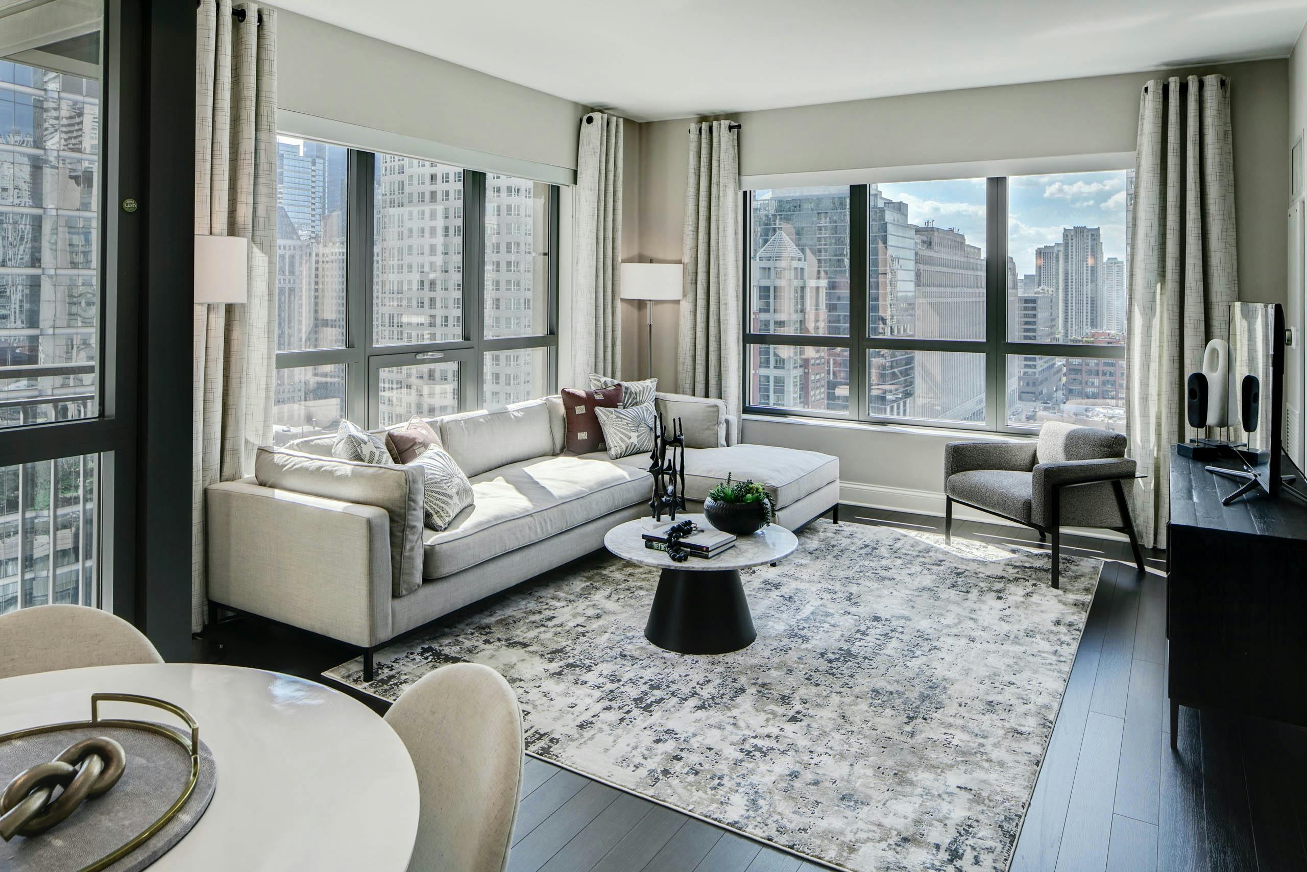 AMLI River North modern apartment living room with neutral furnishings lined with windows showing a vibrant city view