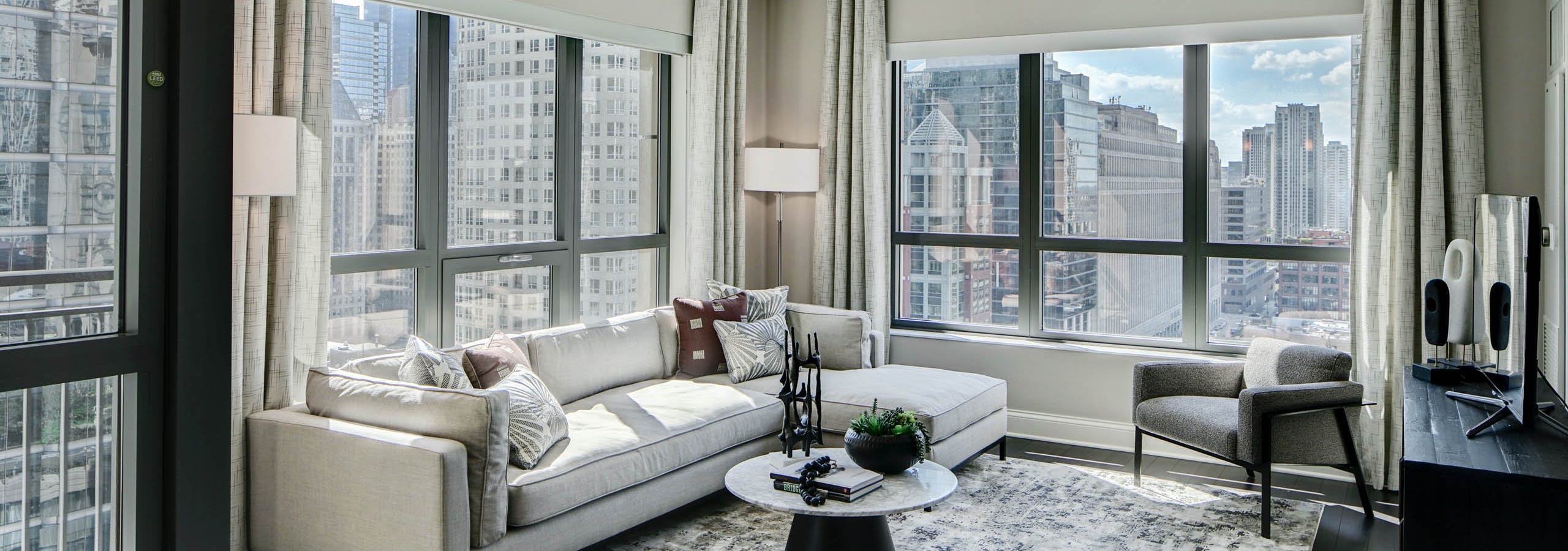 AMLI River North modern apartment living room with neutral furnishings lined with windows showing a vibrant city view