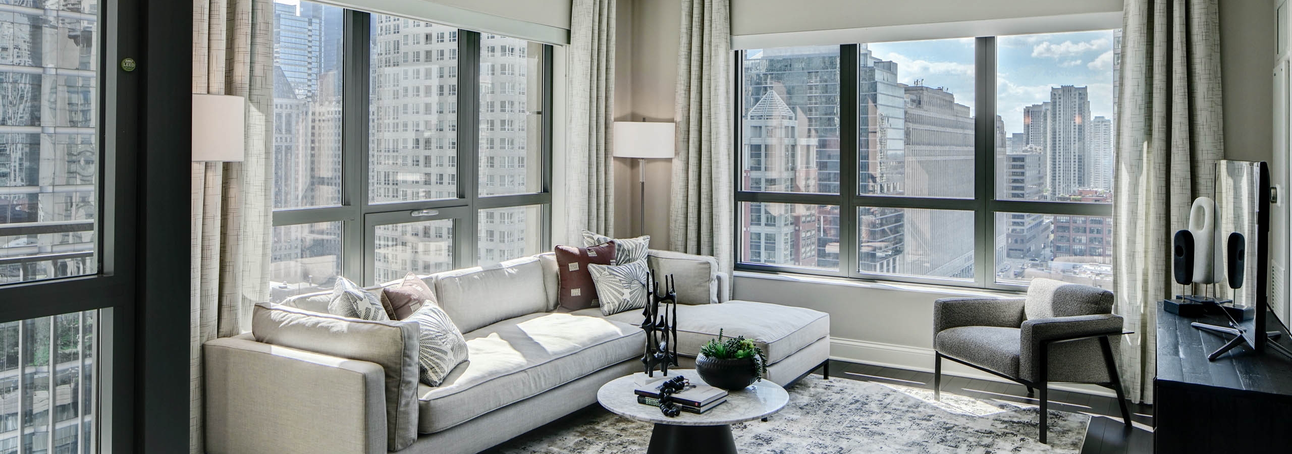 AMLI River North modern apartment living room with neutral furnishings lined with windows showing a vibrant city view