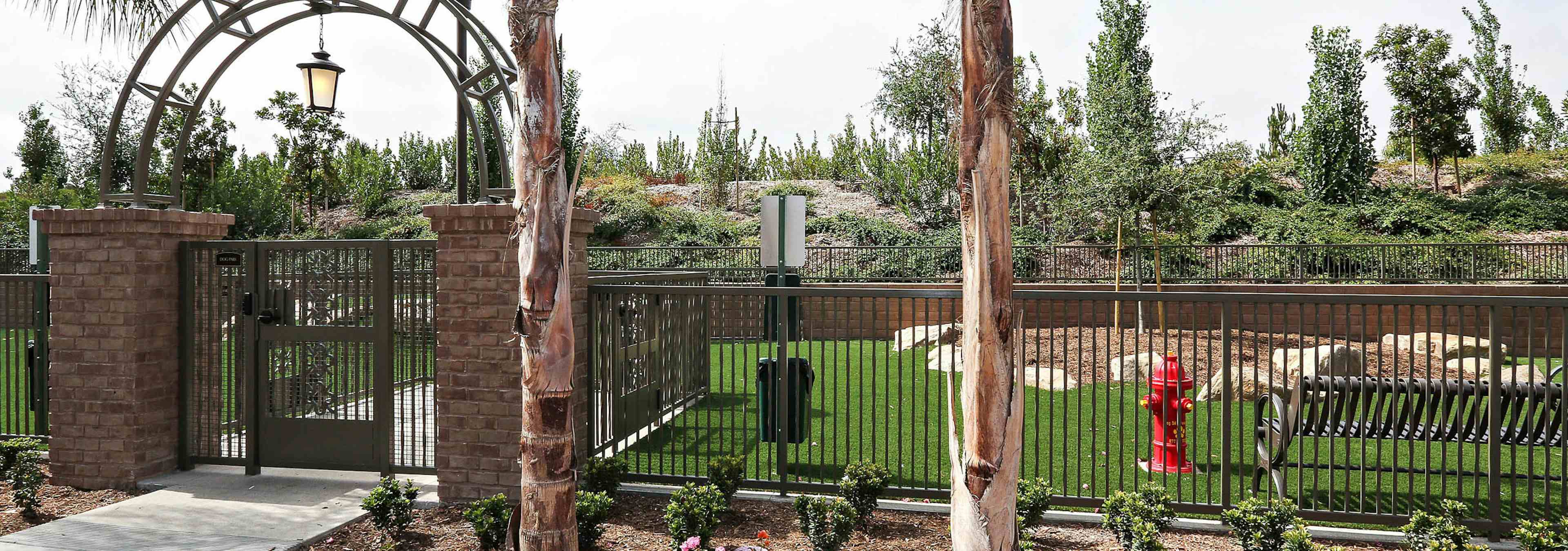 Daytime view of Dog Park’s arched entrance with fence, turf and pet waste station at AMLI Spanish Hills apartment building