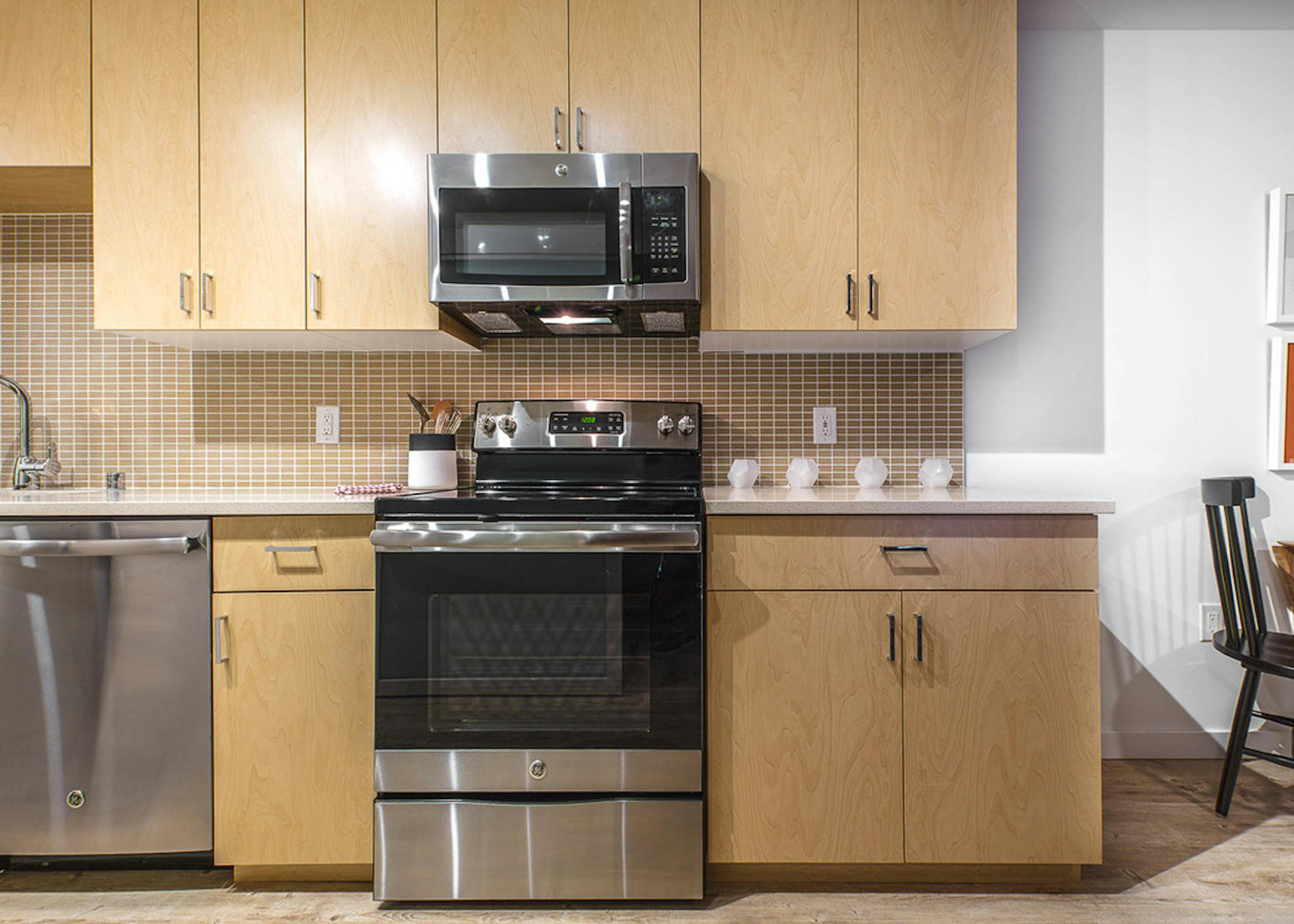 Interior view of an AMLI Wallingford apartment kitchen with light cabinets white quartz counter tops and stainless steel appliances  