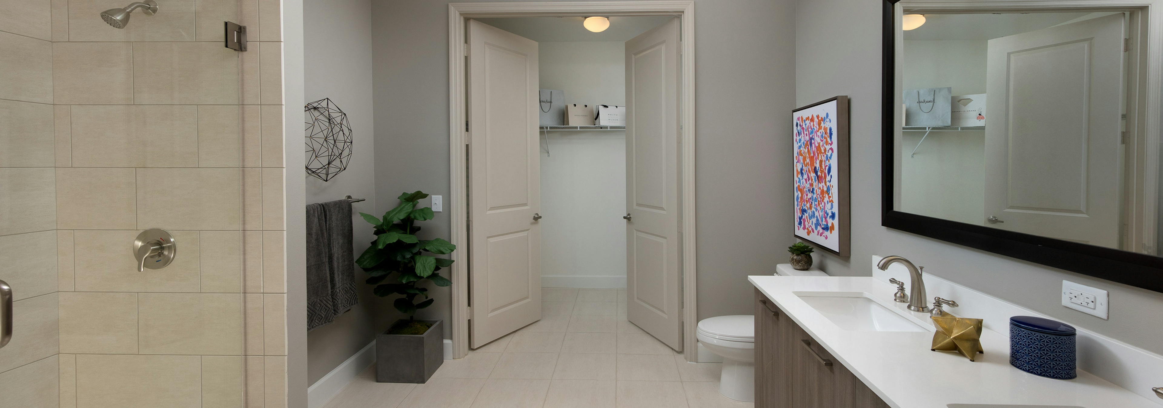 Interior view of AMLI 8800 apartment bathroom with double vanity, mirror, toilet, glass shower enclosure and walk-in closet