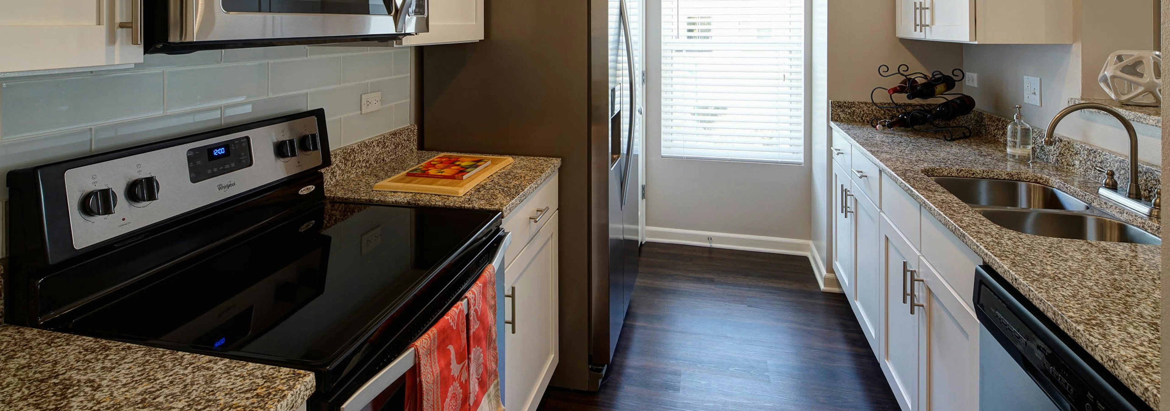 Kitchen at AMLI at Seven Bridges with stainless steel appliances and a white backplash paired with red hand towels