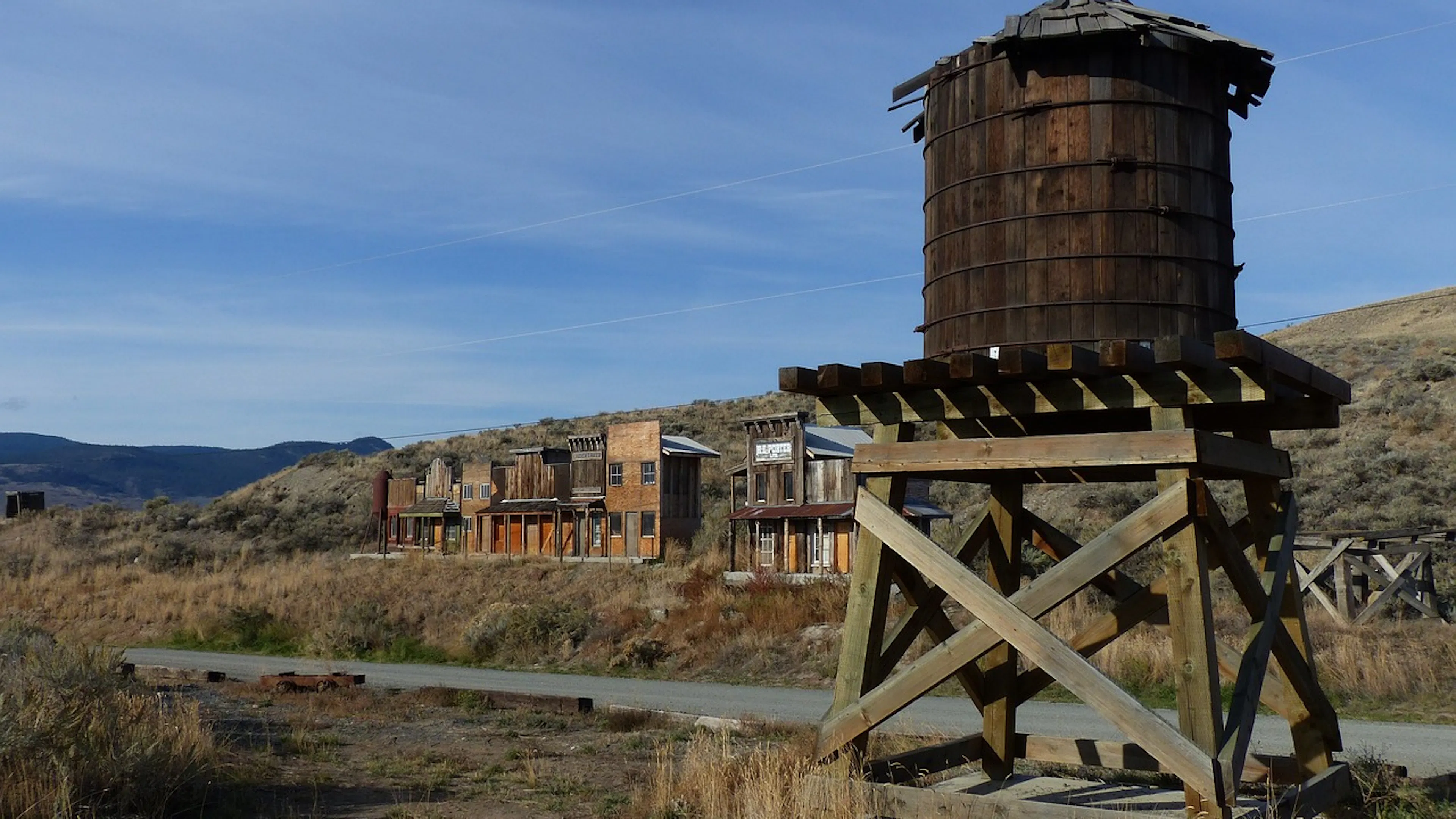 A wooden water tower in the foreground with an abandoned wild west town in the background