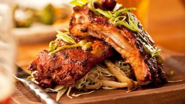 Savory, glazed pork ribs stacked on a rustic wooden platter with sliced green onions and mushrooms.