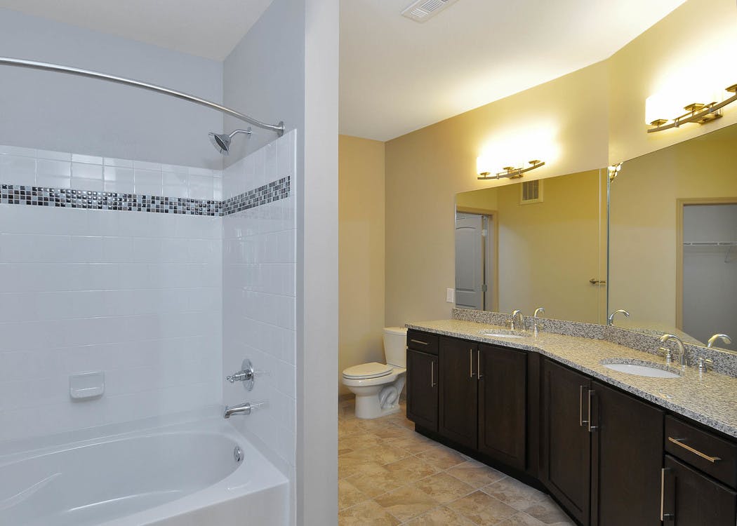 AMLI North Point bathroom with white tiled bathtub and long double vanity sink with dark cabinets and granite countertops