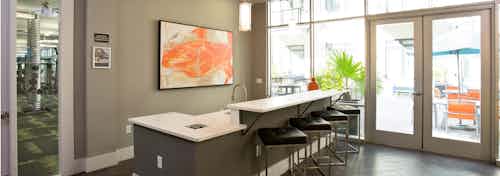 Alternate angle of AMLI 5350 resident lounge with black barstools at a long counter with orange wall art and patio doors