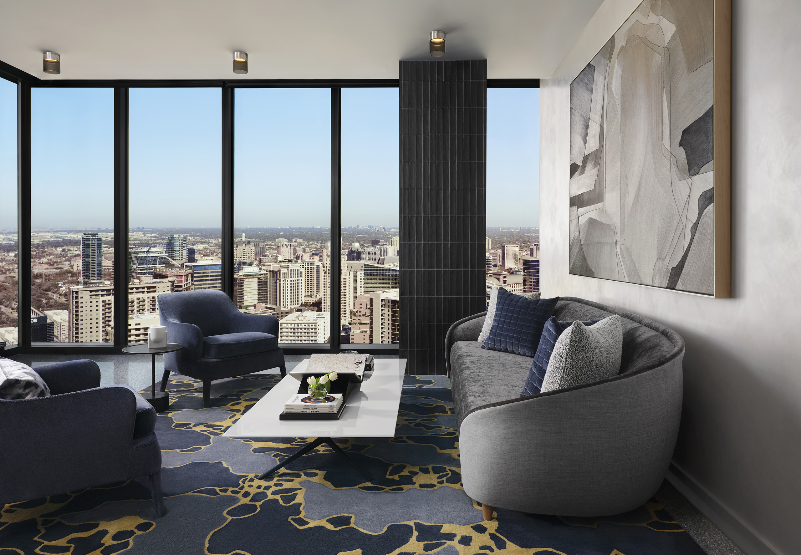 Resident lounge with a plush gray couch and two blue chairs around a coffee table facing expansive skyline view
