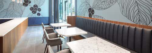 Co working space at AMLI Fountain Place with 3 white tables and long gray booth and blue wall with large brown painted leaves