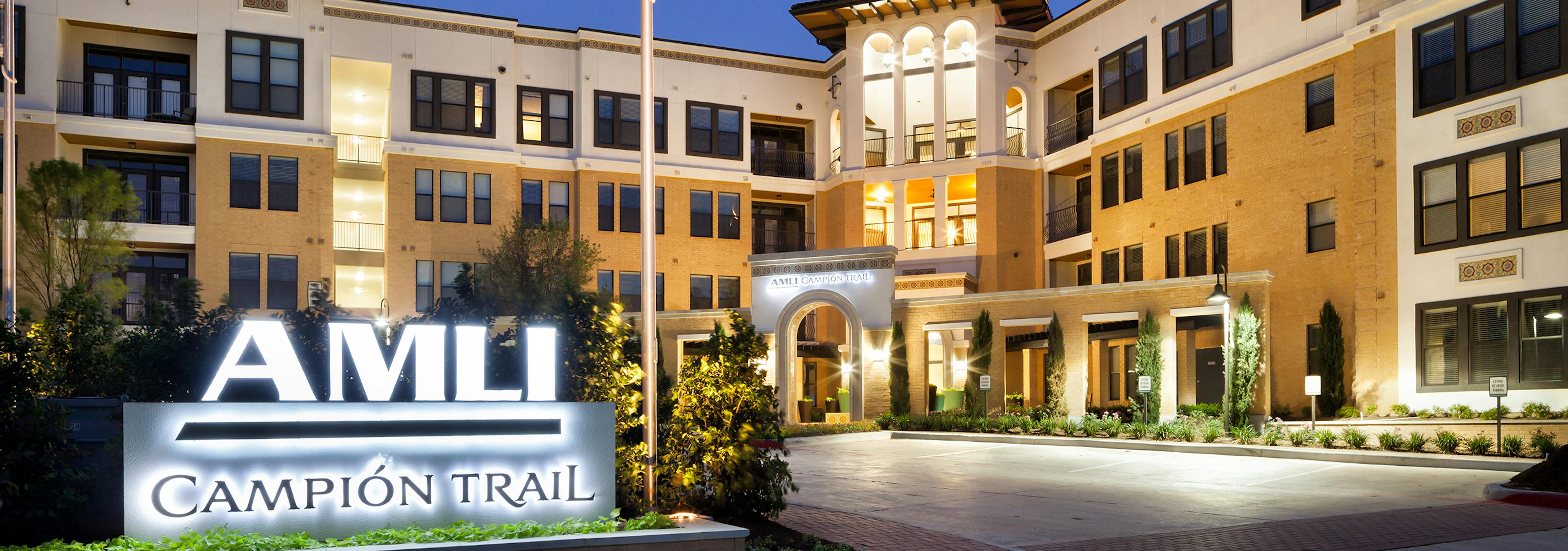 Night view of AMLI Campion Trail orange brick apartment building with sign and flagpole