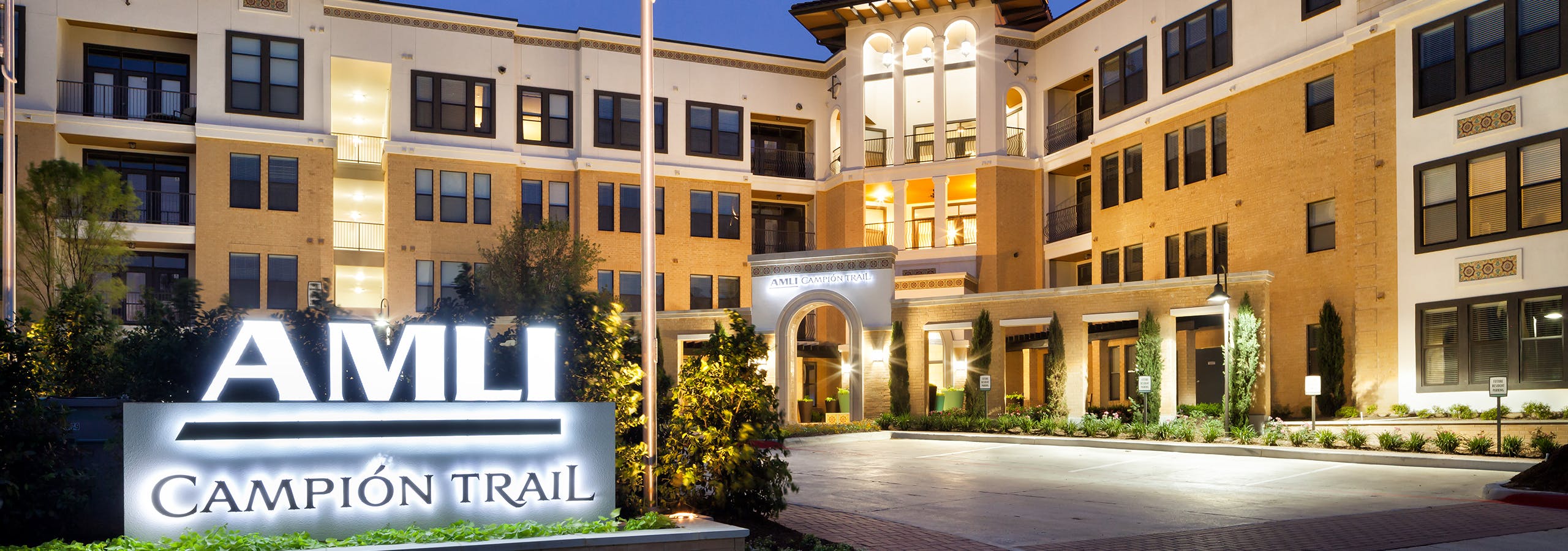 Night view of AMLI Campion Trail orange brick apartment building with sign and flagpole