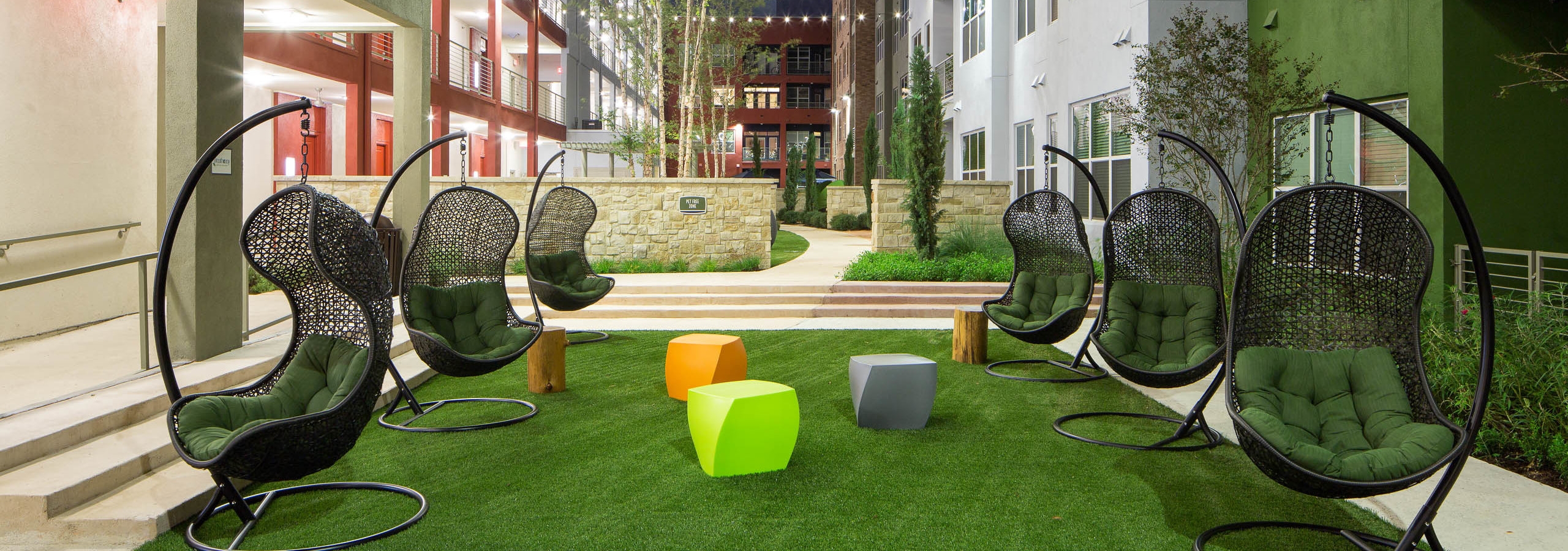 Close up of six green lounge chairs with small colorful tables in the courtyard at AMLI at Mueller at nighttime