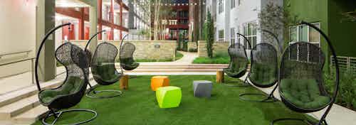 Close up of six green lounge chairs with small colorful tables in the courtyard at AMLI at Mueller at nighttime